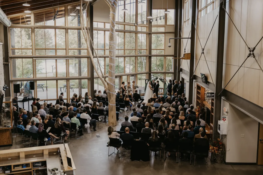 A wide shot from above showing a wedding ceremony in The Nature Place with large windows behind them.